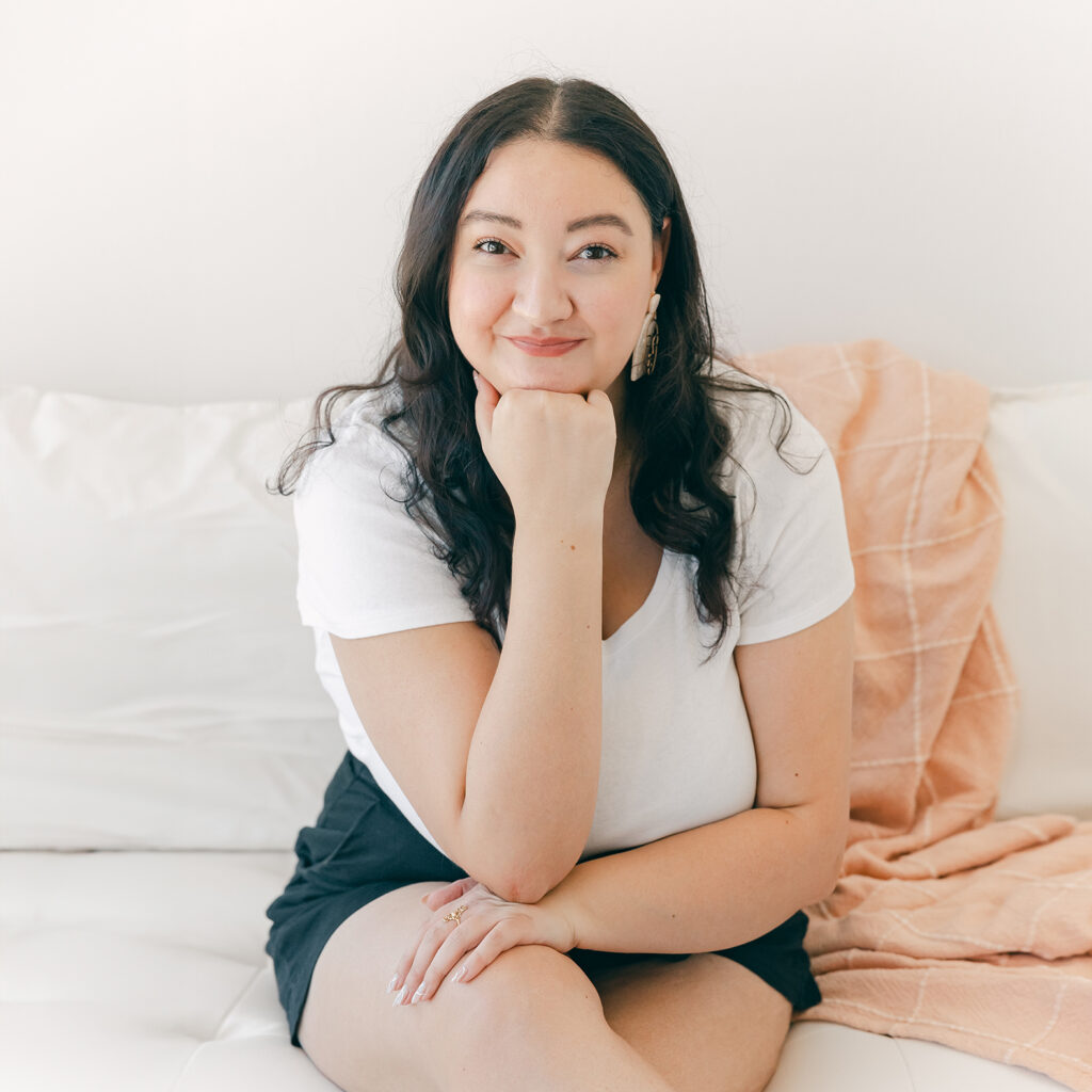 Kimberly sitting on a couch and smiling with her head propped on her hand