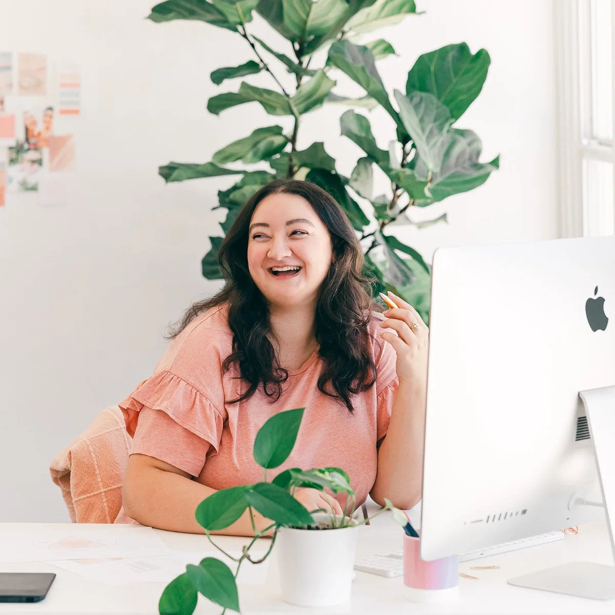 Kimberly at desk working on an iMac and laughing, surrounded by houseplants
